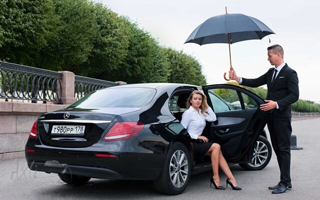 Private Chauffeur holding the umbrella and opening the door to a woman